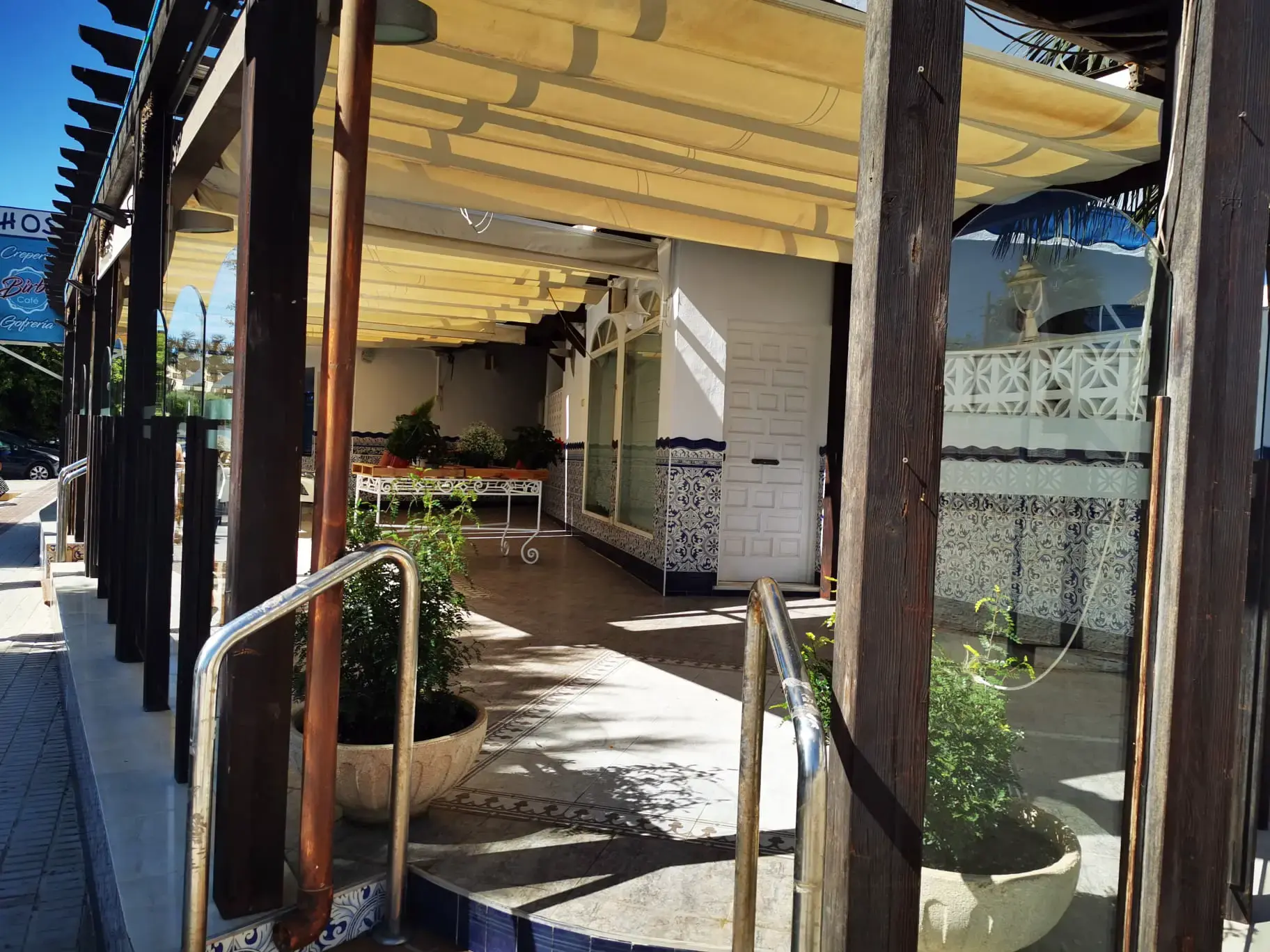 Porche con pérgola de madera, toldo, macetas y zócalo de azulejos junto a la entrada