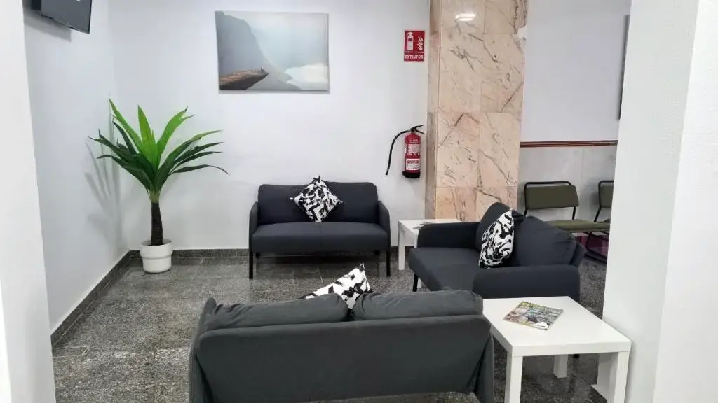 Zona de estar con sofás grises, mesitas blancas y una palmera en maceta