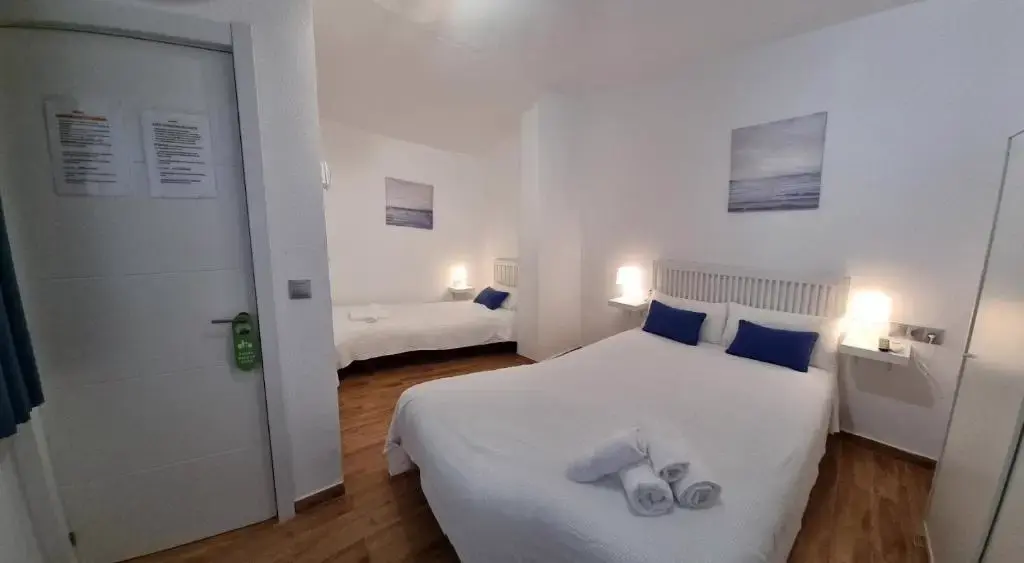 Habitación con cama de matrimonio, cojines azules y una segunda cama al fondo