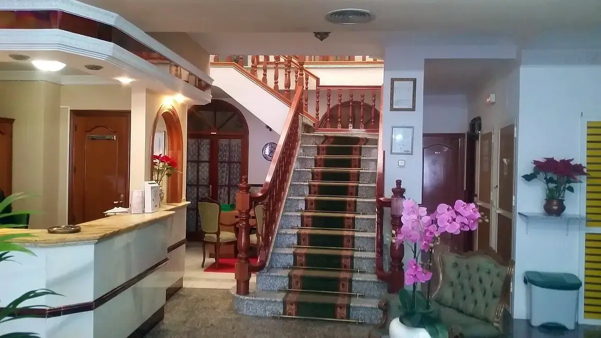 Vestíbulo con mostrador de recepción, escalera de madera con alfombra verde y orquídeas