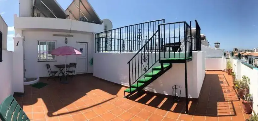 Azotea de baldosa roja con sombrilla rosa, mesa y escalera de forja a un nivel superior