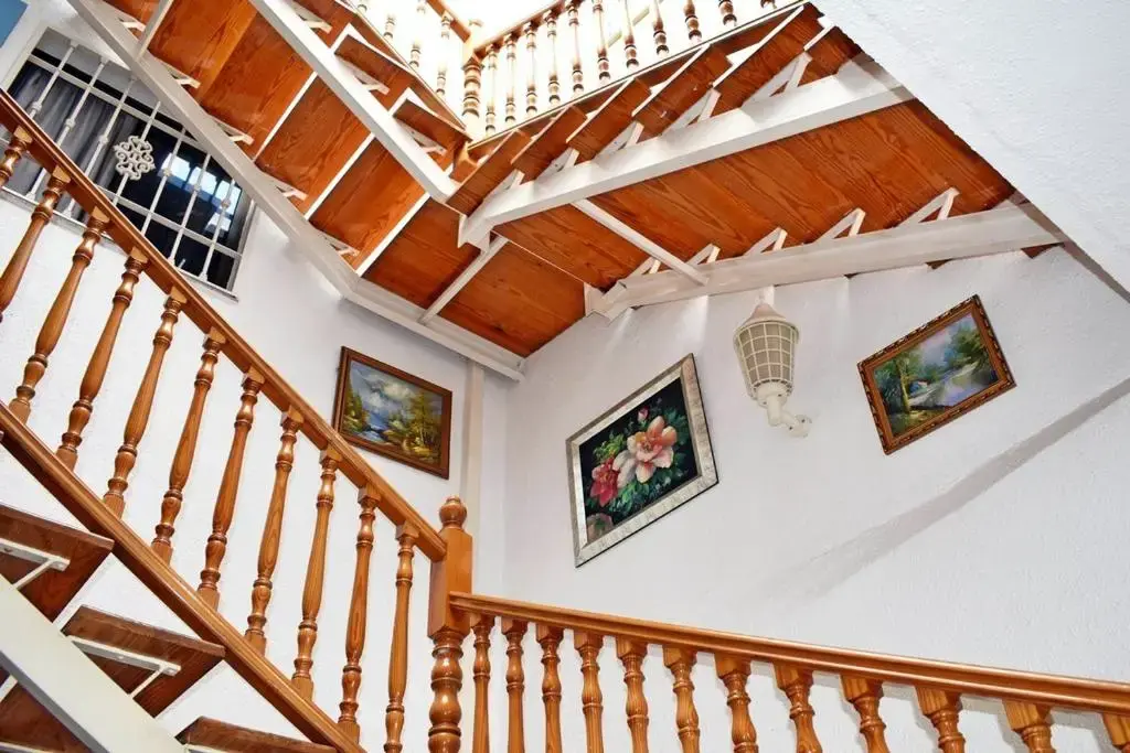Escalera interior con barandilla de madera, techo de tablas y cuadros en las paredes