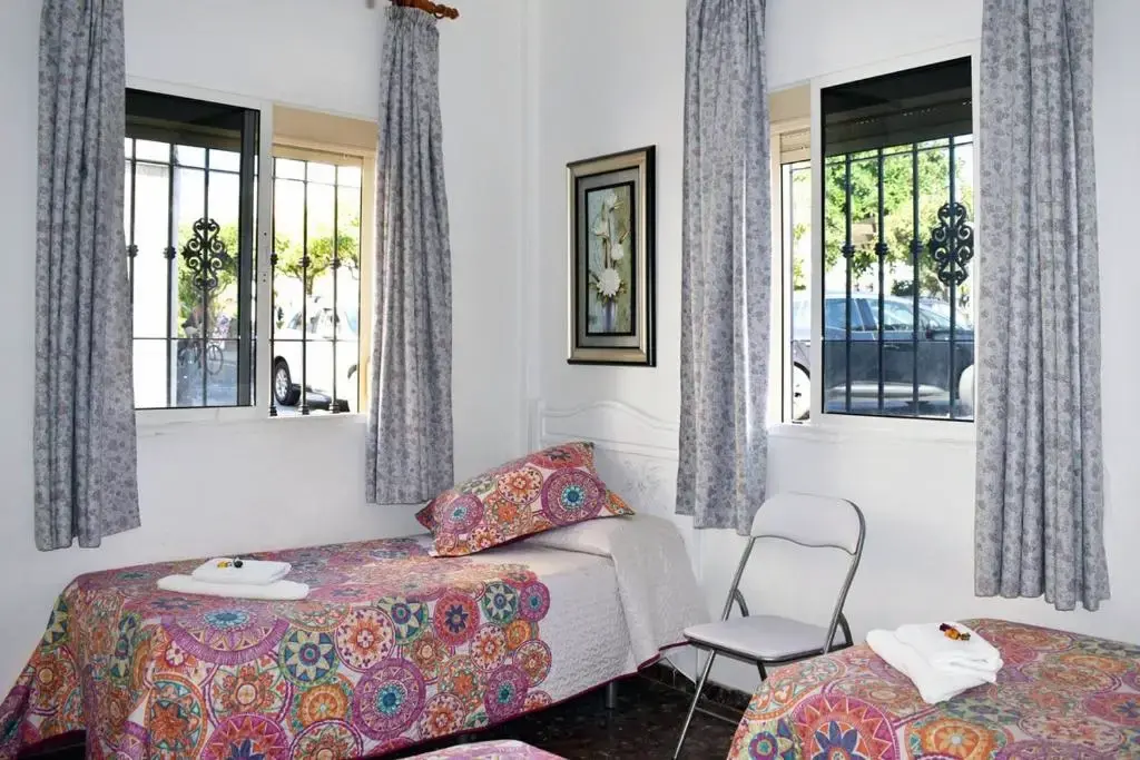 Habitación con camas de colchas estampadas, toallas, silla plegable y ventanas con reja