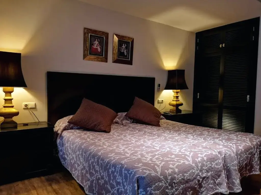 Habitación doble con cabecero oscuro, lámparas de mesa encendidas y colcha estampada