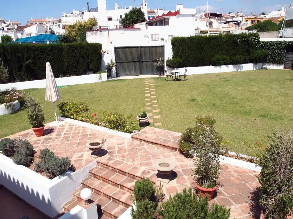 Jardín del hostal con césped, terraza de barro escalonada, macetas y sombrilla cerrada