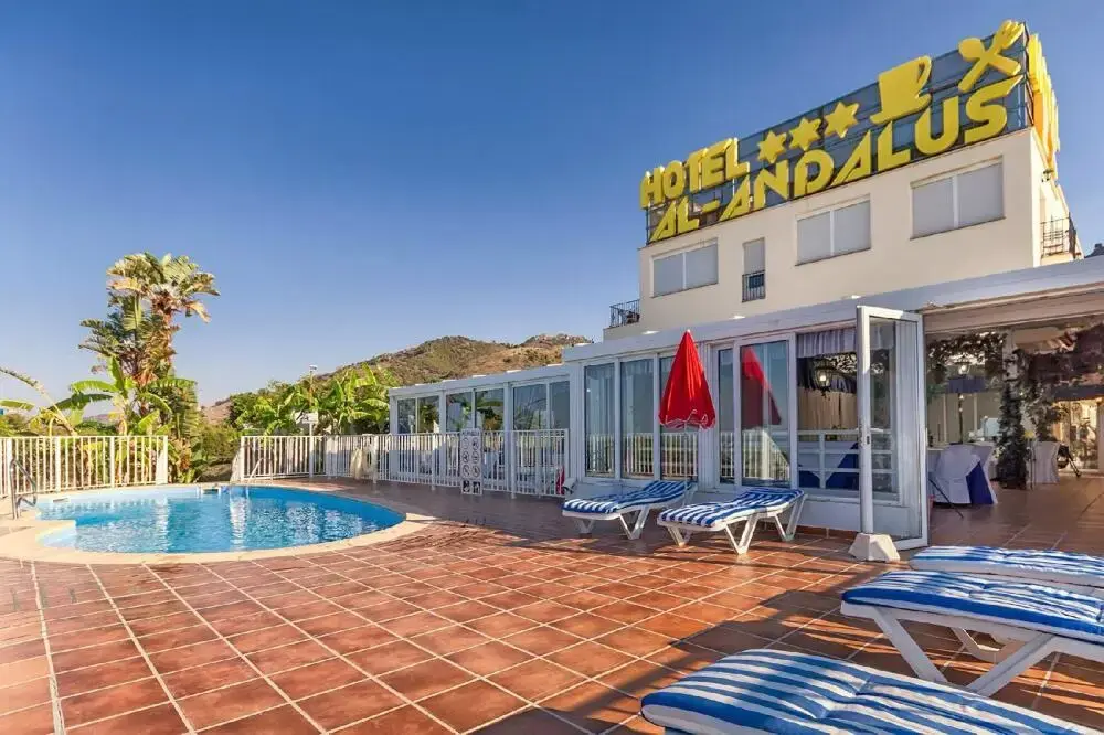 Piscina y solárium con tumbonas junto al edificio del Hotel Al-Andalus y su letrero amarillo
