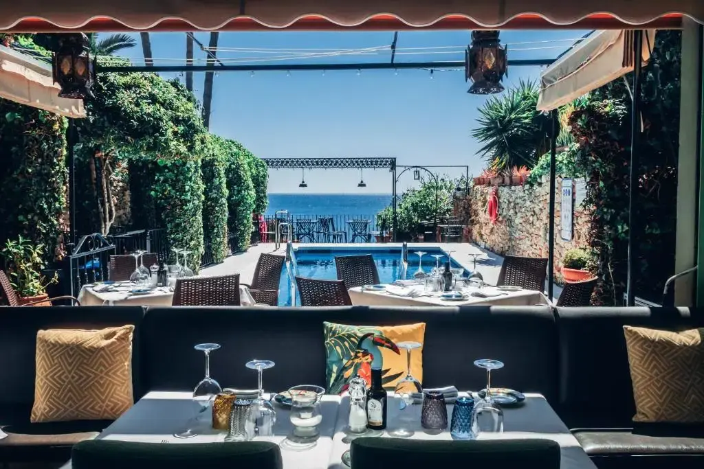Mesas del restaurante con copas y cojines, mirando a la piscina y al mar