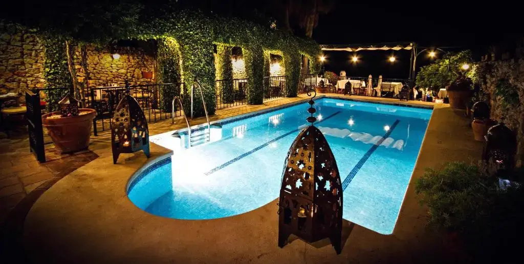 Piscina iluminada de noche con farolillos de estilo árabe y mesas del restaurante