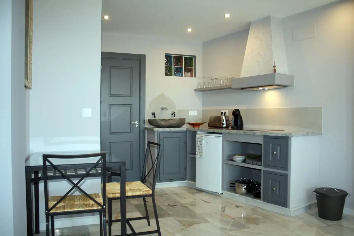 Cocina con fregadero de piedra, campana blanca, nevera pequeña y mesa con dos sillas