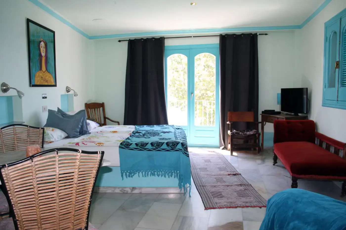 Habitación amplia con cama, colcha turquesa, diván rojo y puerta acristalada al balcón