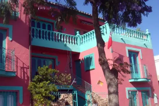 Edificio rosa con balaustradas turquesa, escalera exterior y un árbol delante