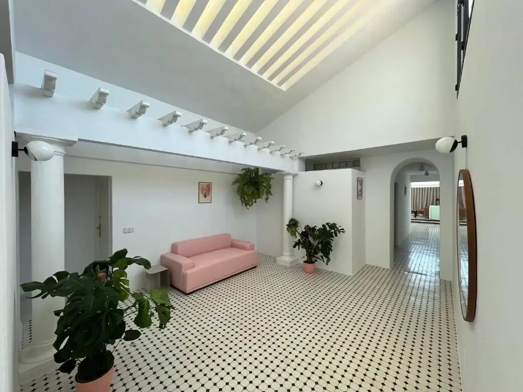 Vestíbulo luminoso con sofá rosa, plantas, columnas y suelo de baldosas blancas y negras
