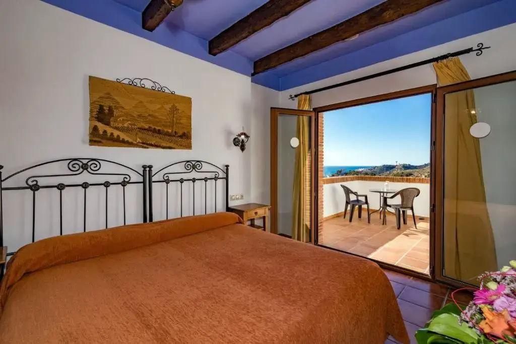 Habitación con cama de matrimonio de forja, techo de vigas y terraza con vistas al mar
