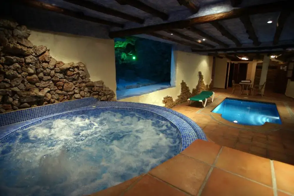 Spa interior con jacuzzi, pared de piedra y pequeña piscina climatizada iluminada