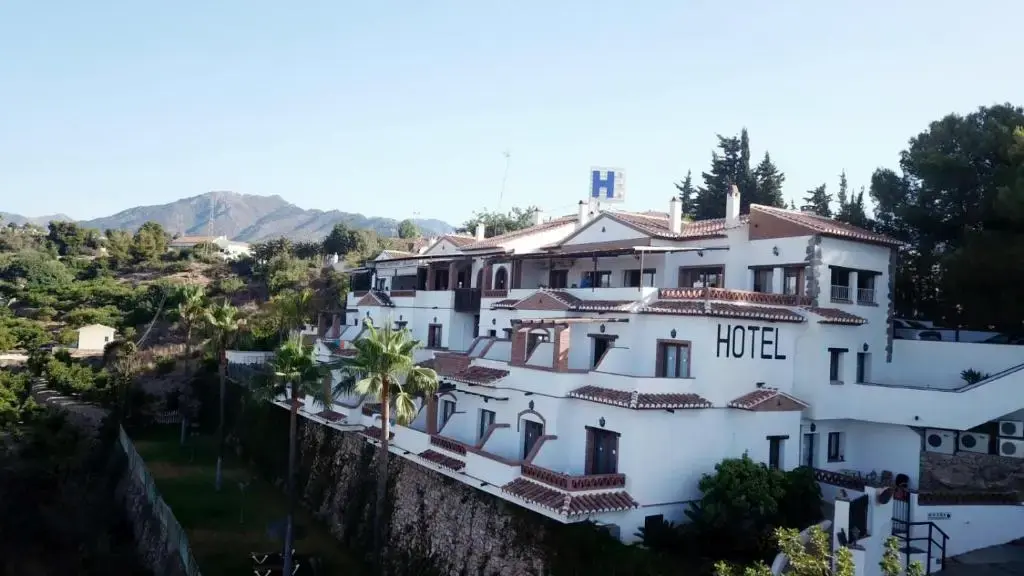 Fachada blanca del Hotel Rural Almazara sobre un muro de piedra, con la sierra al fondo