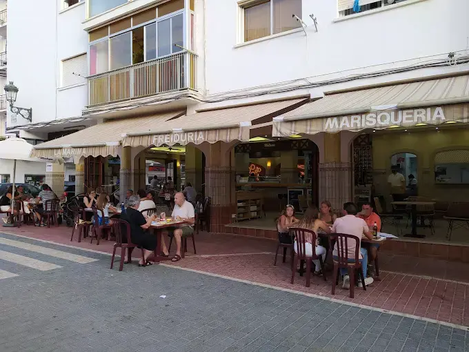 Terraza en la acera al atardecer con clientes cenando bajo los toldos de marisquería y freiduría