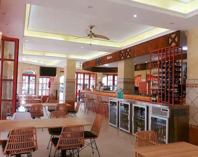 Salón con sillas de mimbre, botellero rojo y neveras de bebidas junto a la barra