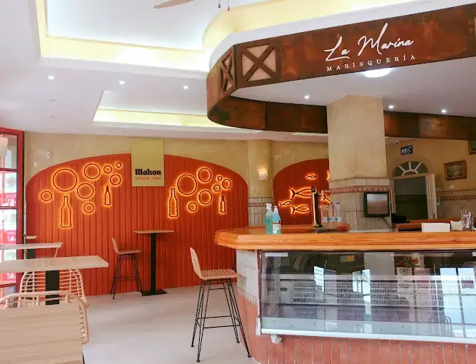 Barra con vitrina y pared naranja decorada con neones de botellas y peces
