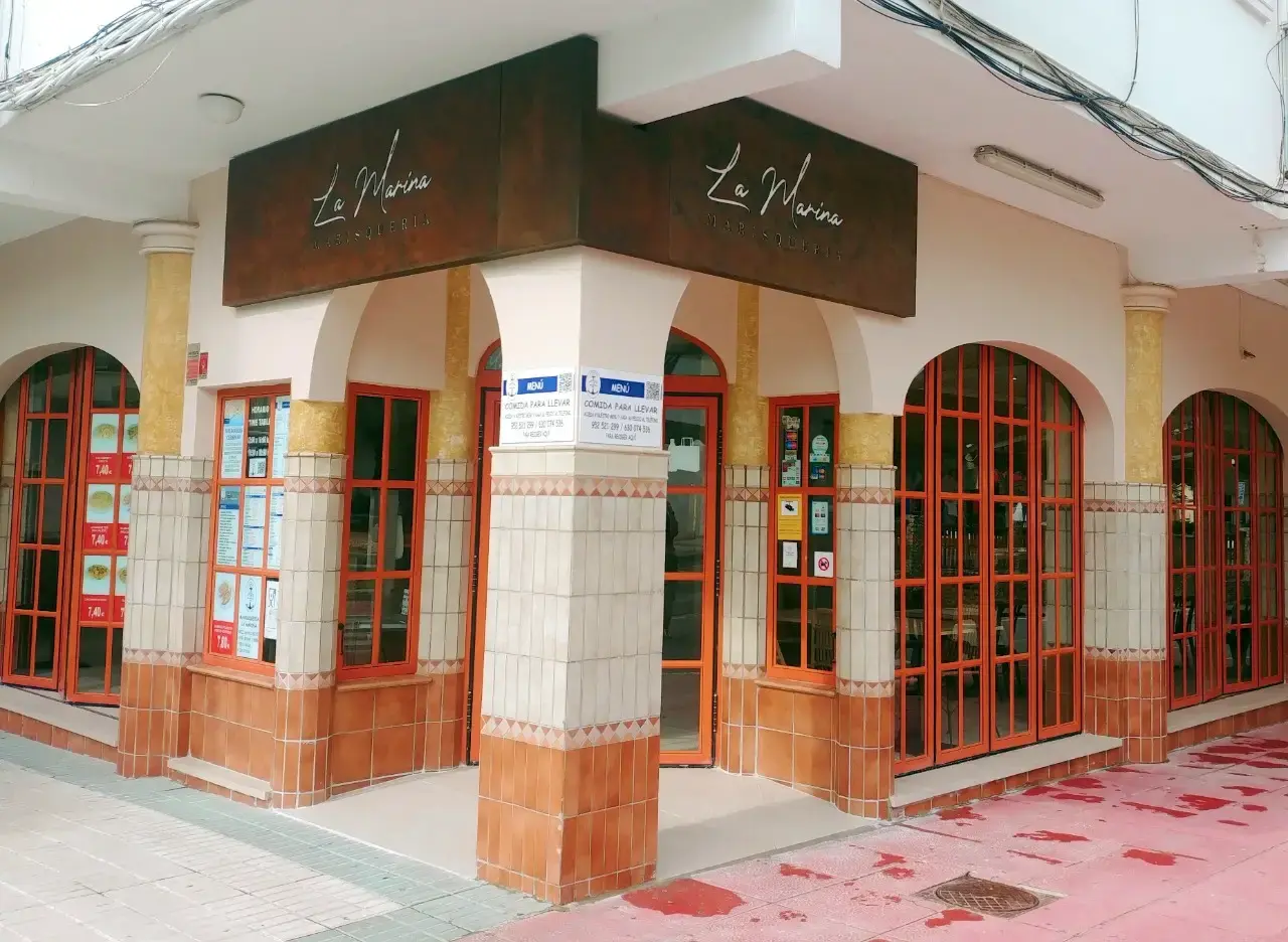 Fachada de esquina con arcos, cristaleras rojas y el rótulo de La Marina
