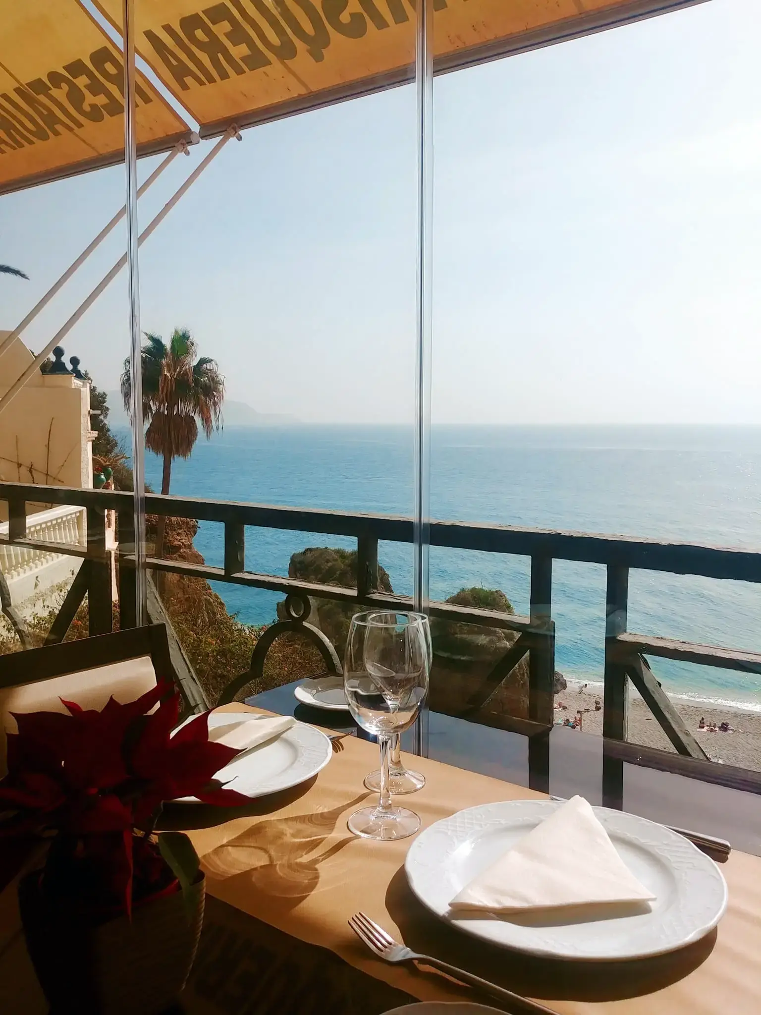 Mesa junto a la barandilla con vistas a la playa y al mar, bajo el toldo de la marisquería