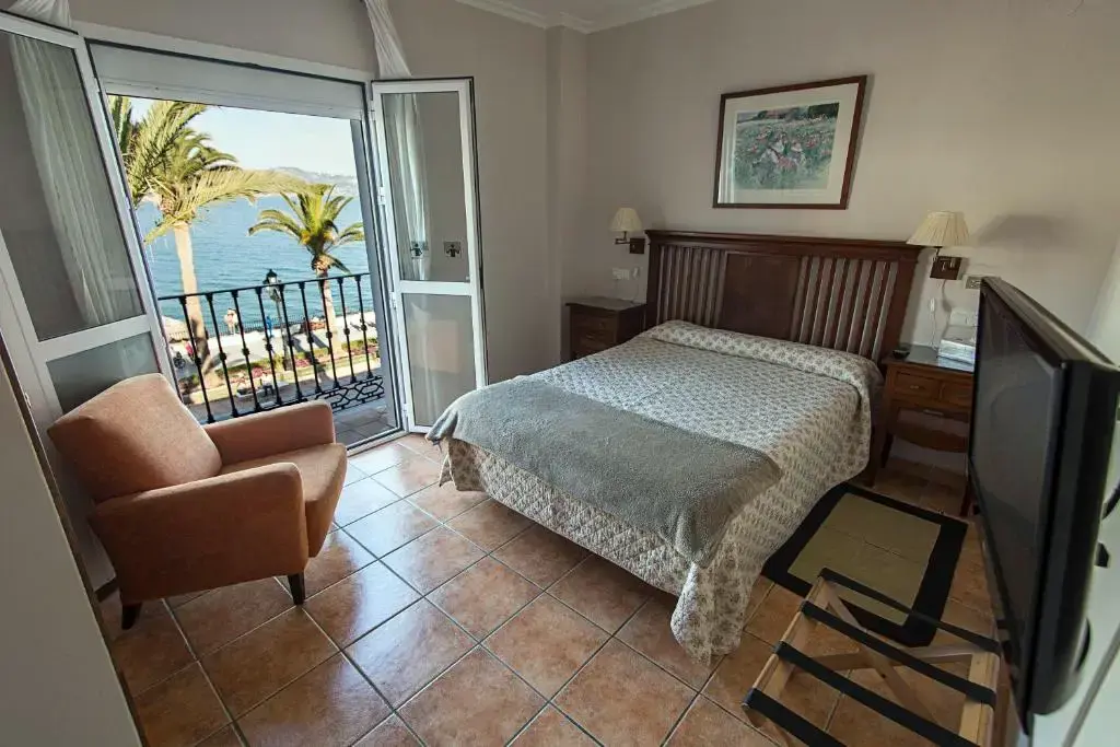 Habitación doble con sillón y balcón abierto a las palmeras y al mar del Balcón de Europa
