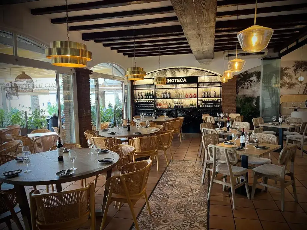 Restaurante con mesas puestas, sillas de rejilla, lámparas doradas y vinoteca al fondo