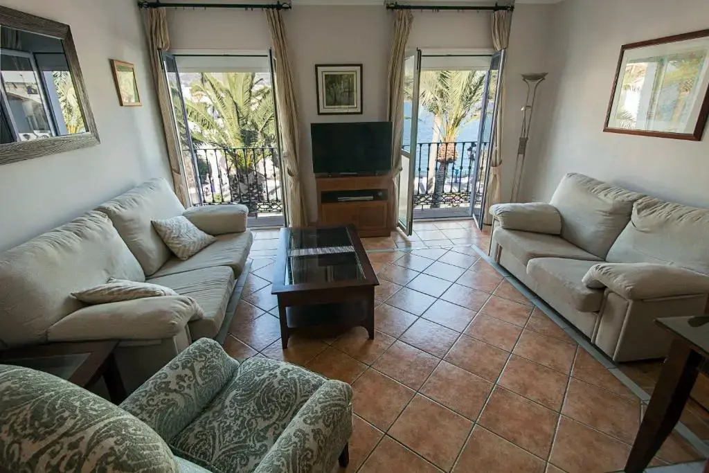 Salón de apartamento con dos sofás, televisión y dos balcones abiertos con palmeras