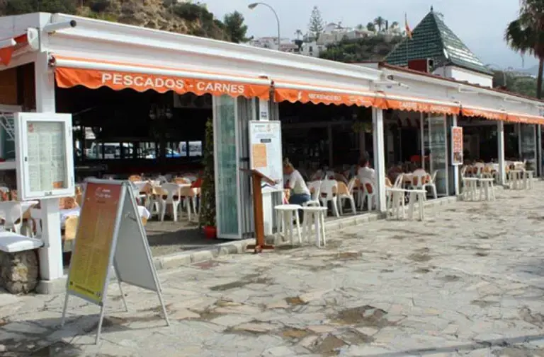 Terraza cubierta con toldos naranjas de pescados y carnes y sillas blancas