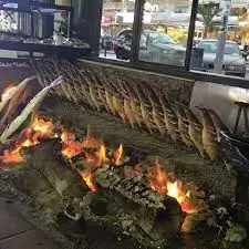 Espetos de sardinas asándose junto a las brasas de leña