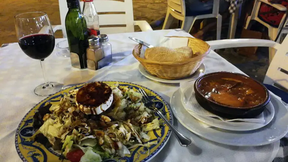 Ensalada con queso de cabra, cazuela con guiso, pan y vino tinto en una mesa