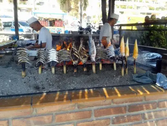 Cocineros asando espetos de sardinas y mazorcas de maíz en la barca de brasas