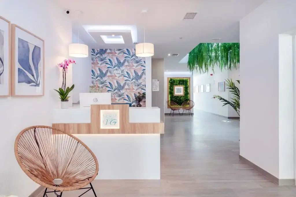 Recepción con mostrador de madera, papel pintado de hojas y jardín vertical en el pasillo