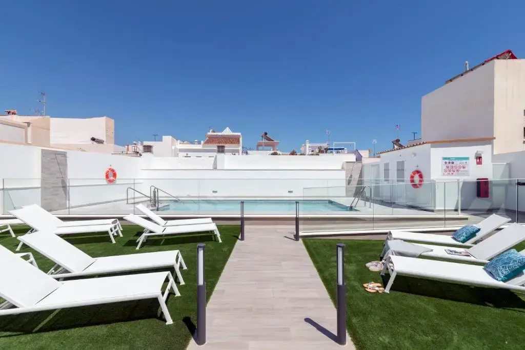 Solárium con césped artificial, tumbonas blancas y la piscina al fondo