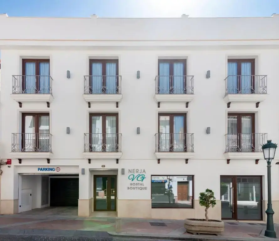 Fachada blanca del Nerja VG Hostal Boutique con balcones de forja y entrada al parking