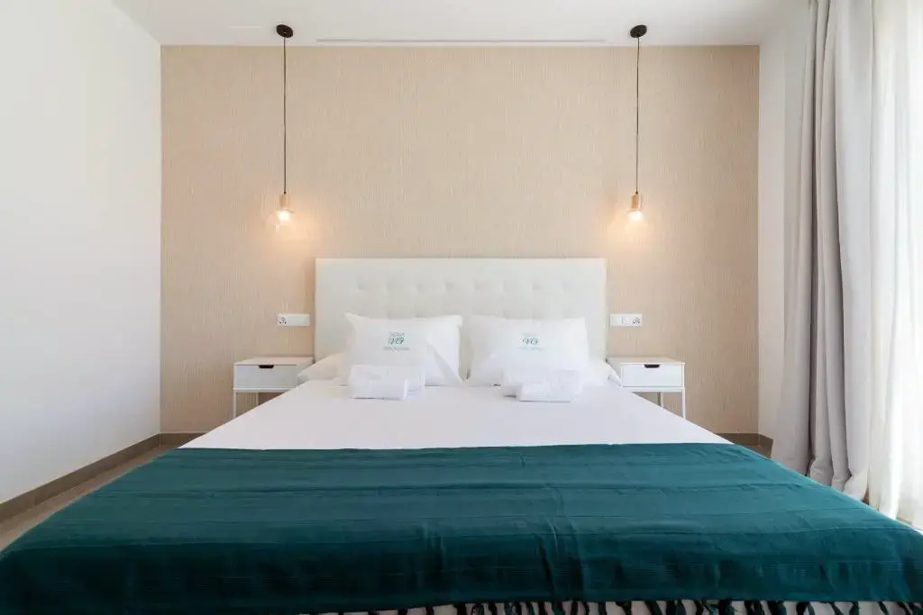 Dormitorio con cama de matrimonio, cabecero blanco acolchado, manta verde y lámparas colgantes