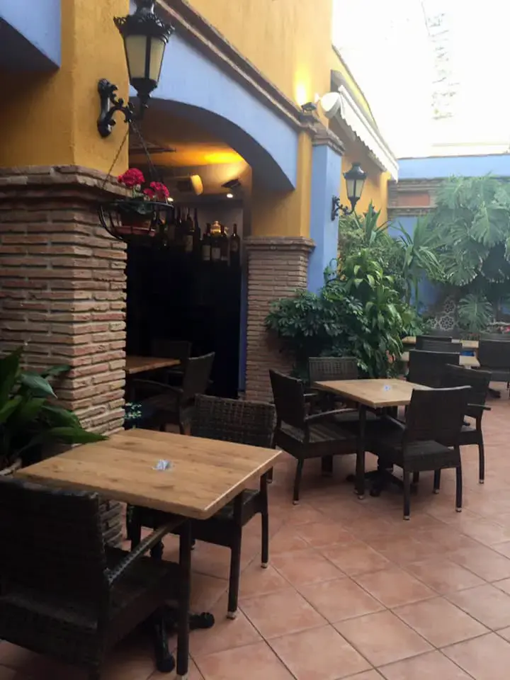 Patio interior con mesas de madera, plantas, faroles y paredes amarillas y azules