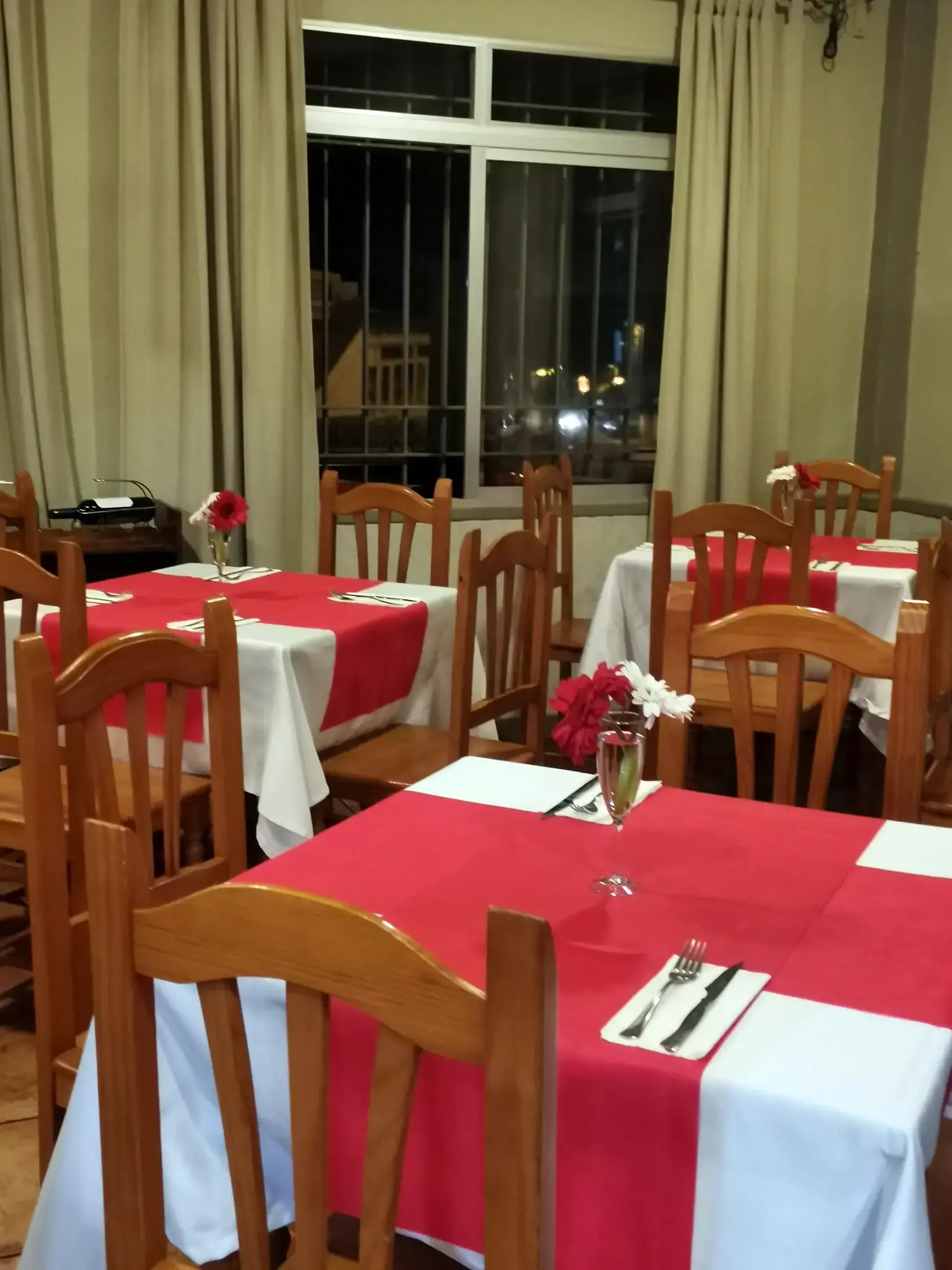 Mesas montadas con manteles rojos y blancos y flores, de noche