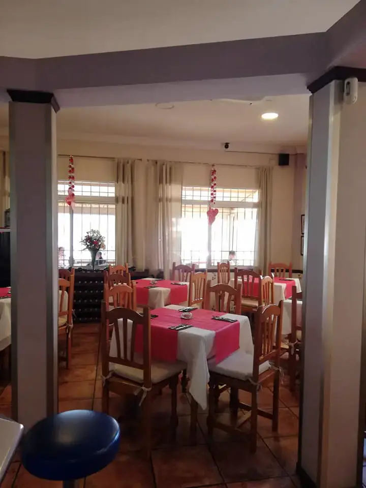 Comedor con mesas de manteles rosa y blanco, sillas de madera y ventanales