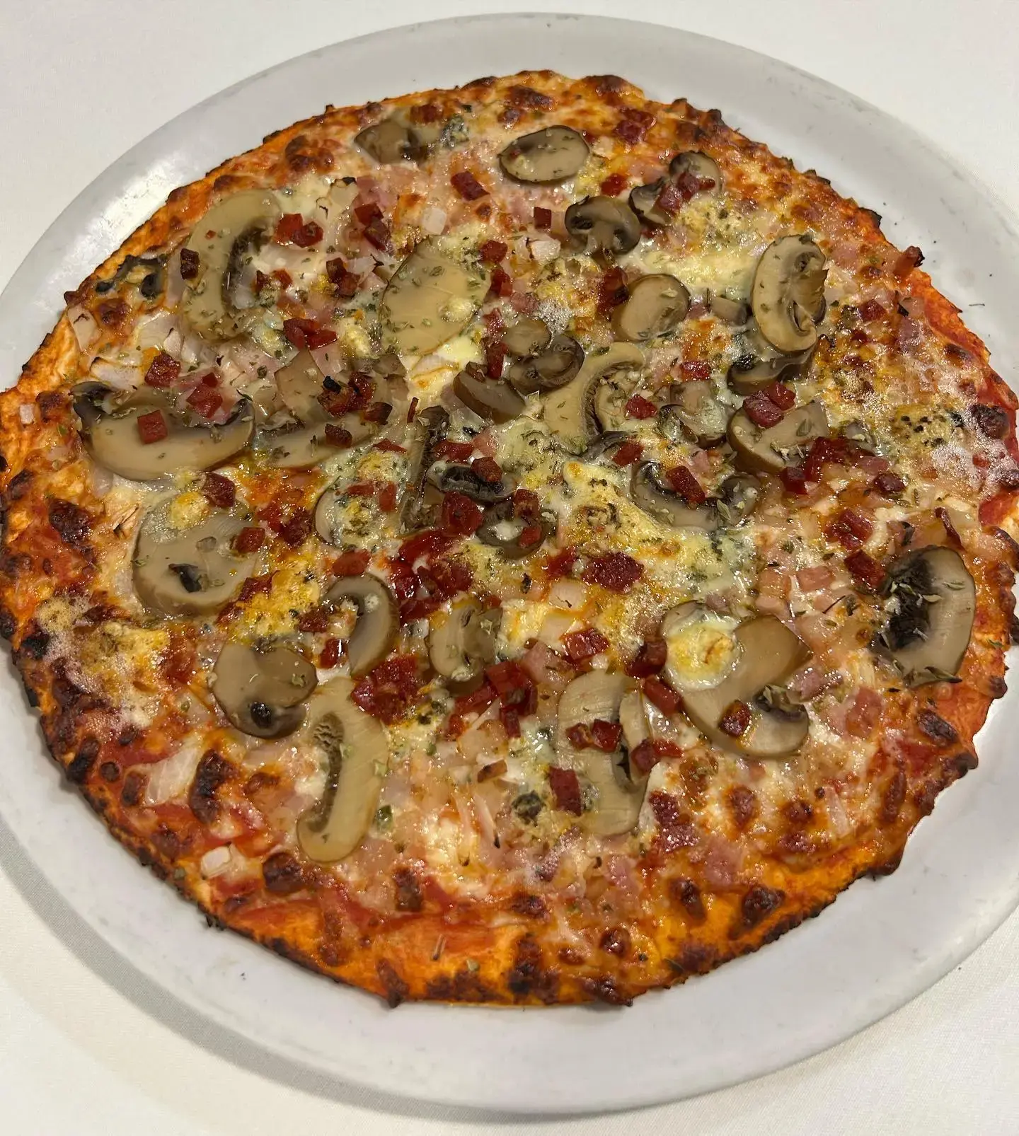 Pizza con champiñones, beicon y jamón en dados sobre plato blanco