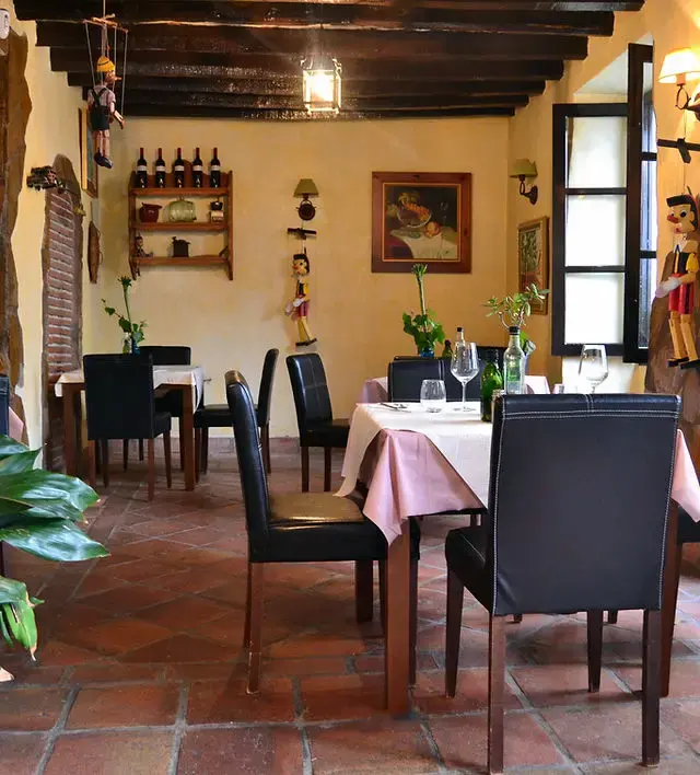Comedor con vigas de madera, suelo de barro y marionetas de Pinocho en las paredes