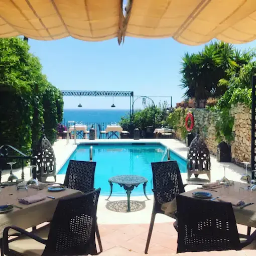 Mesas puestas frente a la piscina con el mar azul al fondo en un día soleado