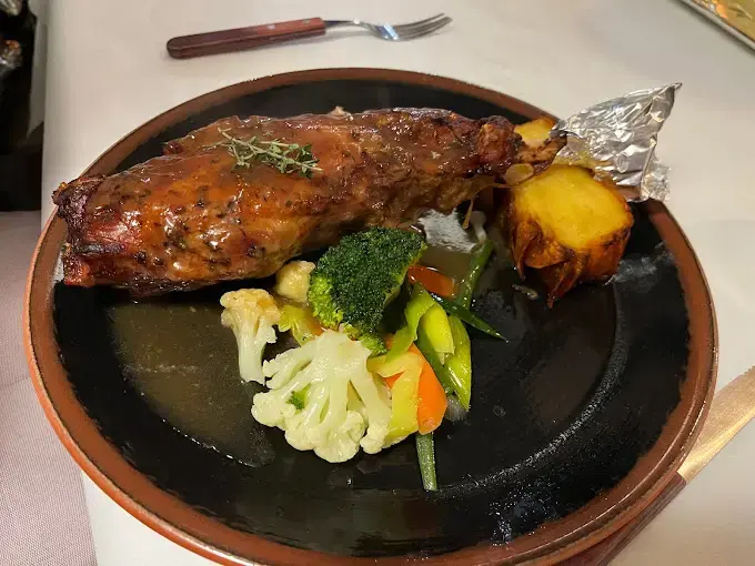 Costillar asado con salsa, verduras salteadas y patata asada en plato de barro