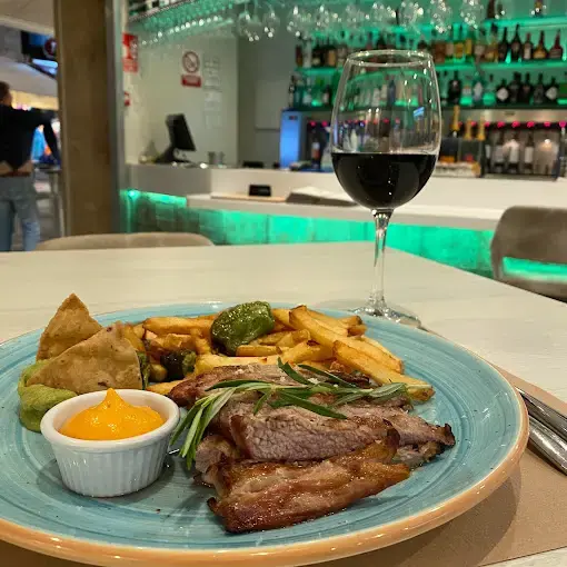 Plato de carne a la plancha con patatas fritas, pimientos y salsa, junto a una copa de vino tinto