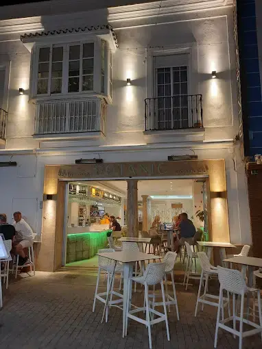 Fachada encalada del Restaurante Botanic de noche, con terraza de sillas blancas en la calle