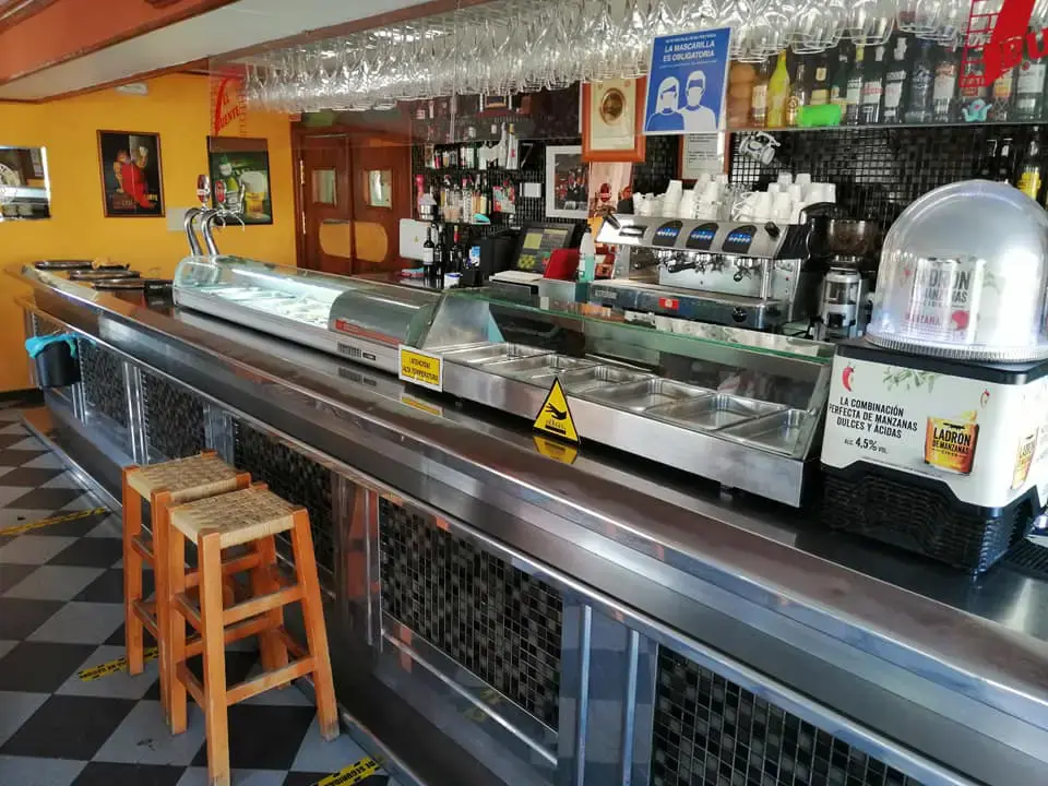 Barra del bar con vitrina de tapas, cafetera y taburetes de madera