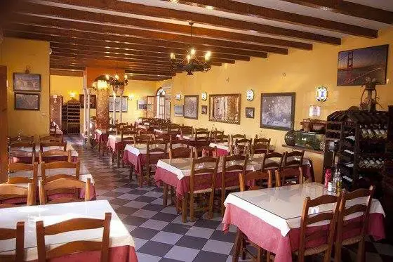 Comedor rústico con vigas de madera, manteles rosas, cuadros y botellero