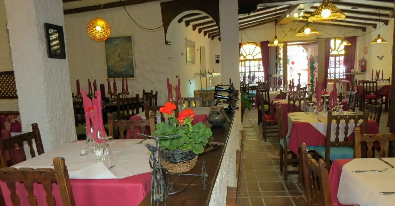 Salón con manteles rojos y blancos, sillas de madera y ventanas en arco