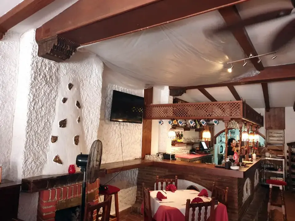 Comedor rústico con paredes encaladas, vigas de madera y la barra al fondo