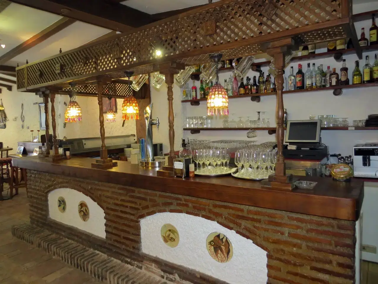 Barra de ladrillo con celosía de madera, lámparas colgantes y botellero