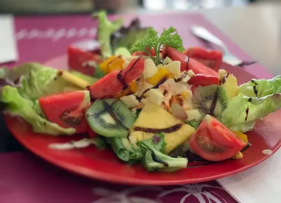 Ensalada de lechuga con tomate, kiwi, piña y queso en un plato rojo
